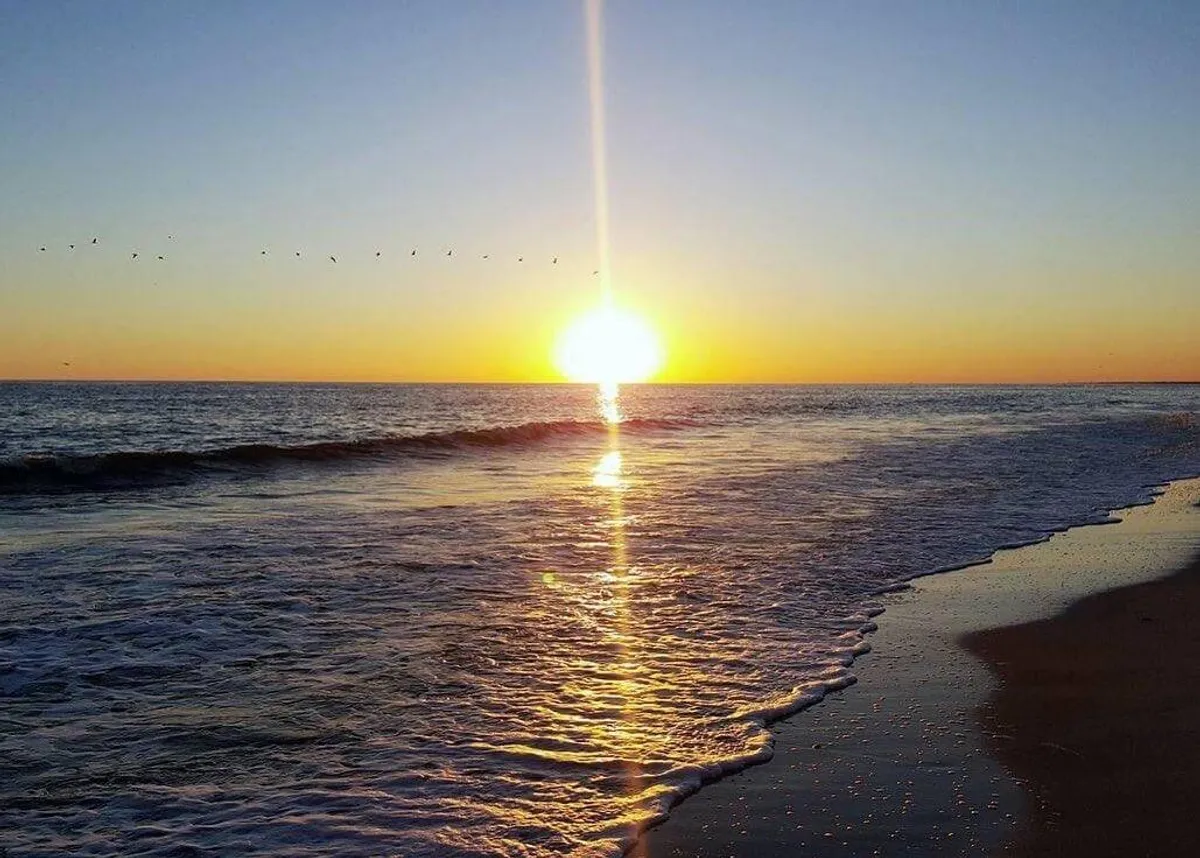 A picturesque oceanfront view at sunset, featuring gentle waves, soft sandy shoreline, and a tranquil atmosphere. The scene invites relaxation and hints at the direct beach access available from the property.