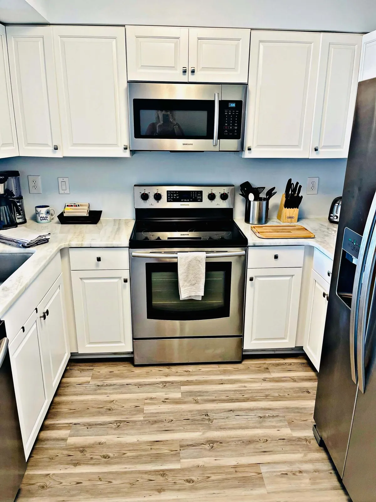 This image features a warm, welcoming kitchen space with gleaming stainless steel appliances, a marble countertop, a wooden cutting board, and a utensil holder. The overall ambiance is inviting and suggests both functionality and a homely feel ideal for family gatherings and meal preparation.