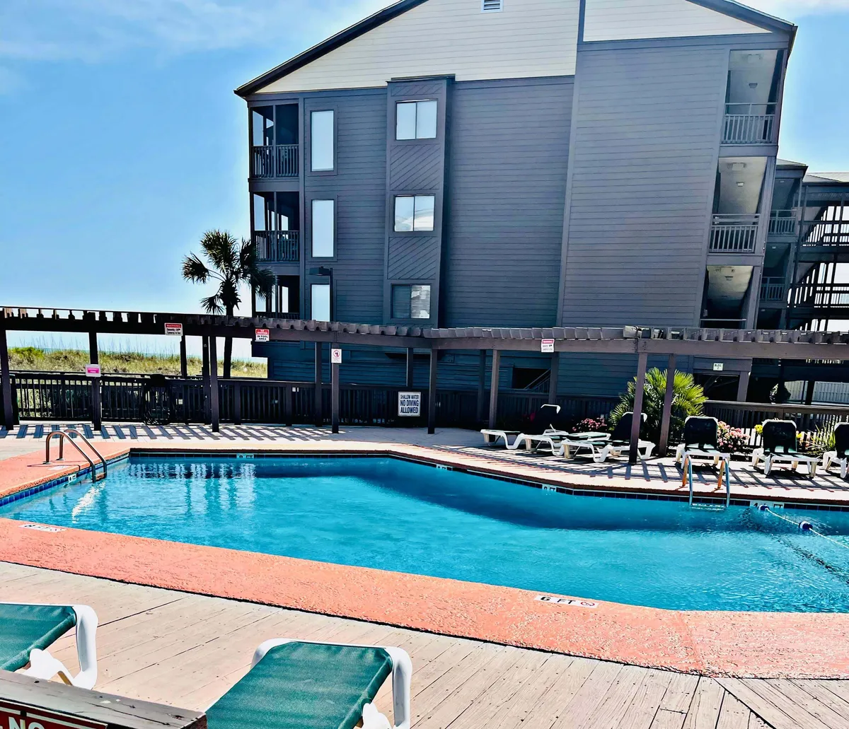 A sunlit pool scene with inviting lounge chairs, swaying palm trees, and the building’s facade in the background. The atmosphere is vibrant and social, highlighting both the pool's welcoming design and the easy access from the condo units.