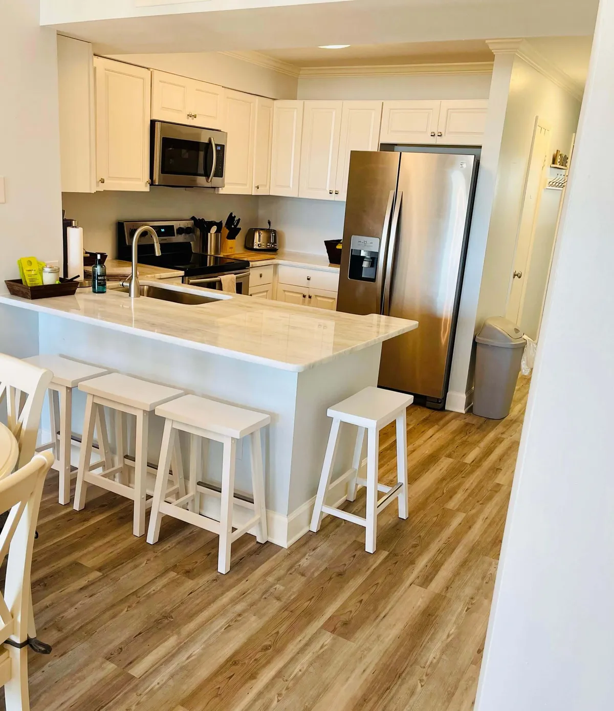 A spacious kitchen scene with a central island featuring seating, complemented by stainless steel appliances and light wooden flooring. The island offers casual dining and gathering space, perfect for entertaining or a quick breakfast before a beach day.