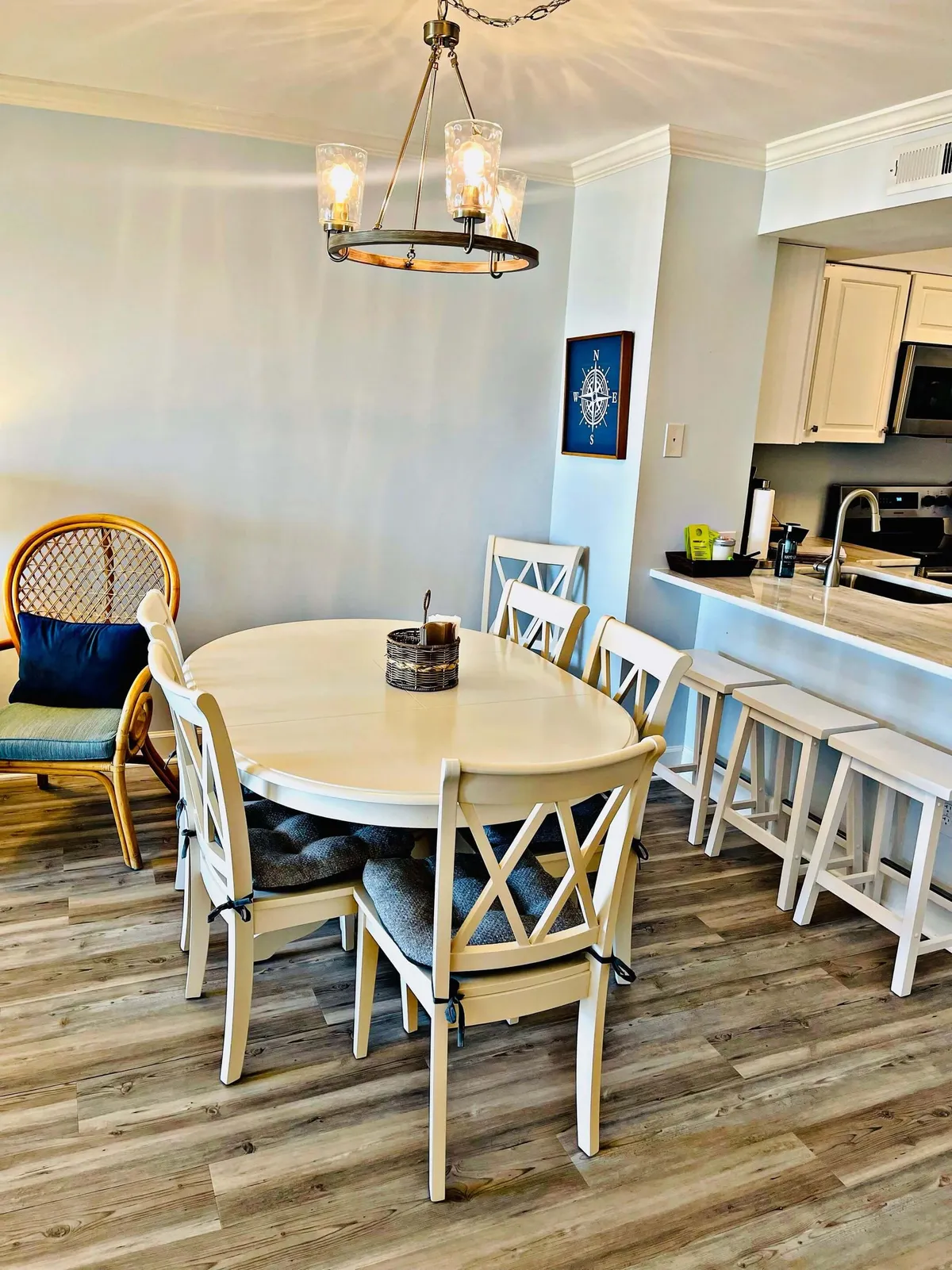 A welcoming dining area featuring an oval table set beneath a stylish chandelier, with woven chairs and decorative wall art. The space exudes warmth and is perfectly arranged for family meals, celebrations, or casual get-togethers.